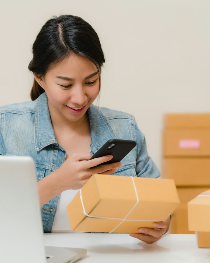 Empreendedora sorrindo enquanto confere um pedido no celular antes de despachar a caixa